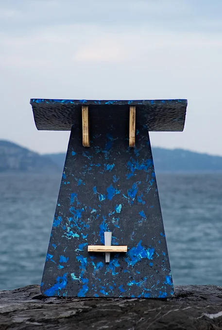 Tabouret en plastique recyclé bleu et bois, posé sur un rocher face à la mer