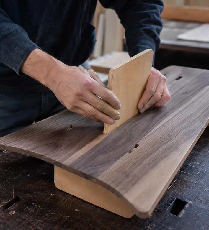 Les mains d’un menuisier ajustant une pièce de bois sur un plateau, à l’établi